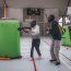 Two people playing indoor paintball wearing masks and using inflatable barriers for cover.